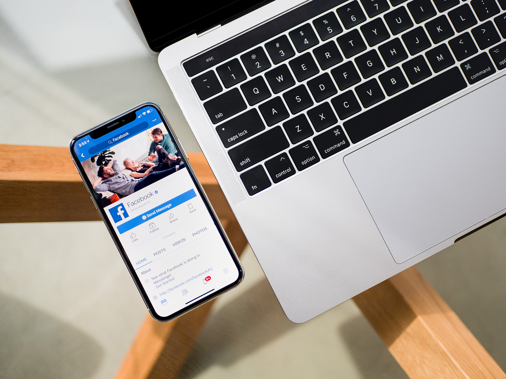 Cell phone showing social media sitting on a table next to a laptop.